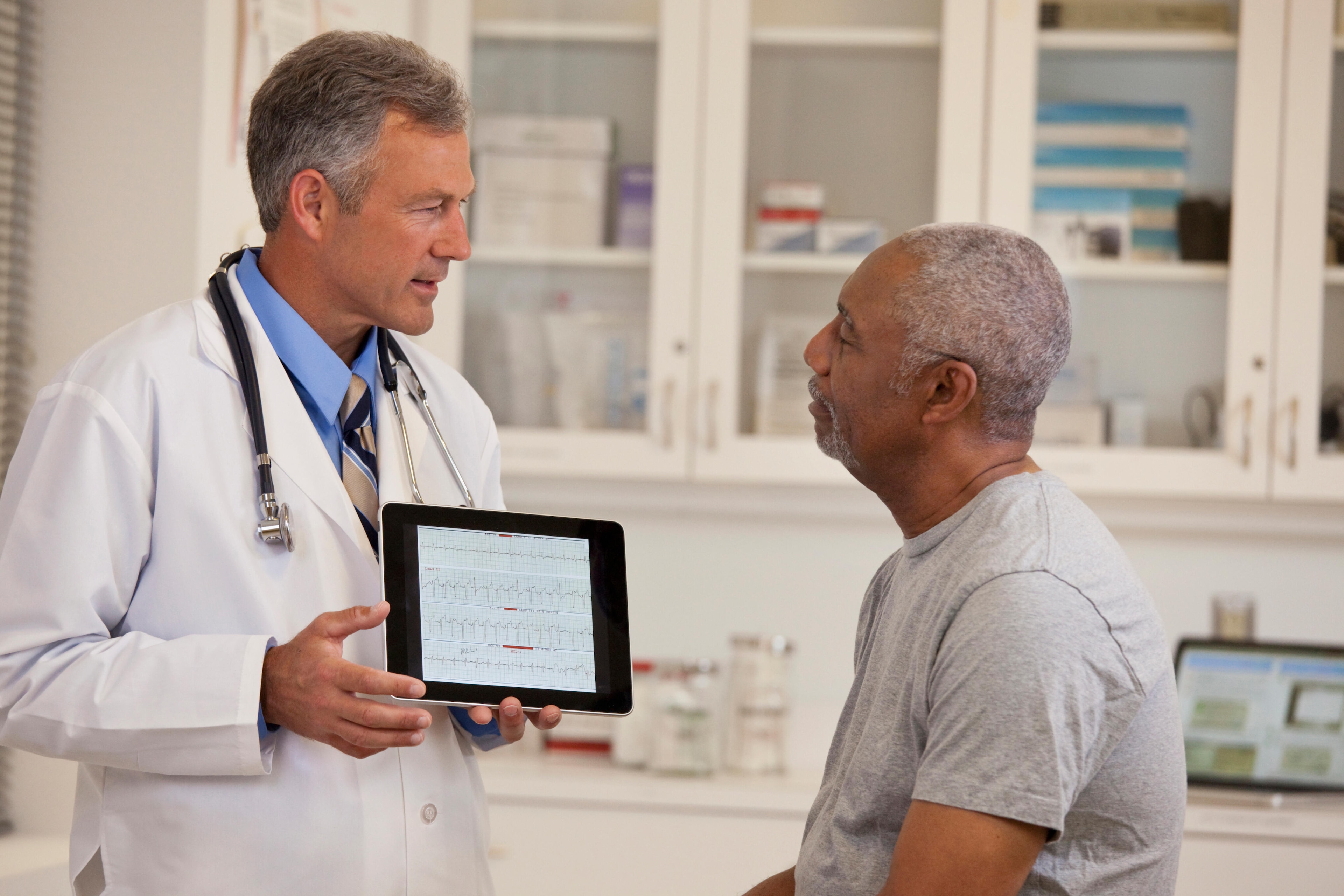 Un médico conversa con un hombre mayor en un entorno clínico, mostrando una gráfica de resultados clínicos de cáncer de tiroides en un tableta