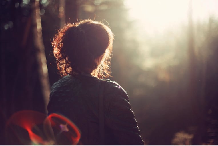 Mujer observando el sol en el bosque, rodeada de naturaleza y luz.
